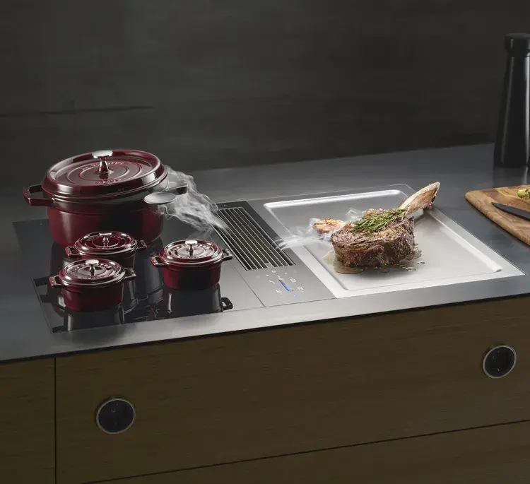 Drei rote Pfosten auf einer Induktionskochplatte, daneben wird Lammsteak gebraten.